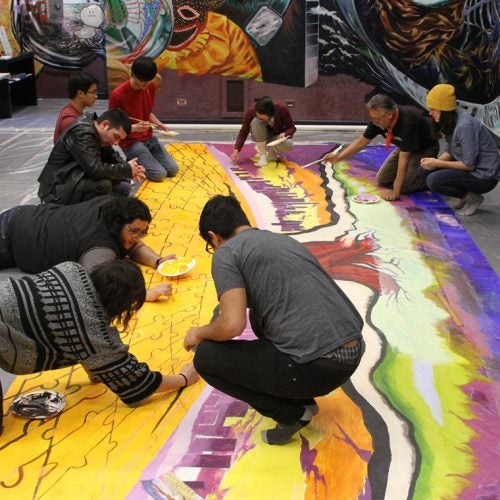 Latino Cultural Center community collaborates on painting a mural on the ground.