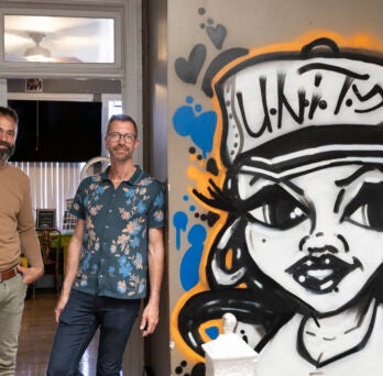 Robert Difazio and Brent Talbot standing next to a graffiti painting of a woman wearing a cap that says 