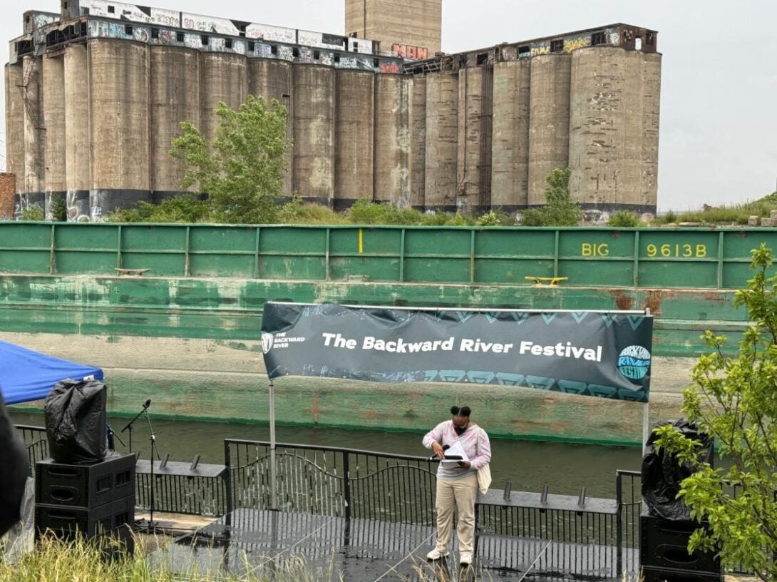 A single person stands beneath the banner of the Backward River Festival. The massive Damen Grain Silos tower in the background.