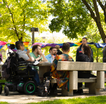 Attendees of the Pride Picnic seated at the grassy patio area behind the Behavioral Sciences Building 