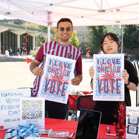 Two kiosk workers holding signs for voter registration